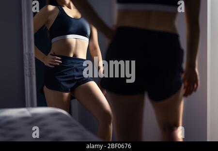 Fortschritte und Ergebnisse in Gewichtsverlust, Training, Fitness oder Ernährung. Perfekte gesunde schlanke Körper. Fit Frau schaut sich nach dem Sport in den Spiegel. Stockfoto