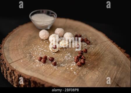 Hausgemachte Süßigkeiten weiße Schokolade, Kokosnuss und Haselnüsse auf einem Stück Holz. Schneeball mit Bonbons Stockfoto