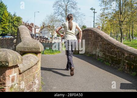 Kidderminster, Großbritannien. April 2020. Da Großbritannien in seiner vierten Woche der Lockdown wegen des Coronavirus, die Menschen halten ihre Stimmung auf und während die Sonne weiterhin scheint, sorgen sie dafür, dass sie immer noch raus zu trainieren einmal am Tag. Diese isolierte junge Dame, von hinten gefangen, macht einen flotten Spaziergang durch einen Stadtpark. Bild: Lee Hudson Stockfoto