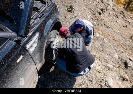 Kaukasus, Georgien, Tusheti Region, Omalo. Zwei Männer stellten einen Wagenheber auf, um einen Platten Reifen auf der Straße nach Omalo - Tusheti mit Bergen im Hintergrund zu reparieren Stockfoto