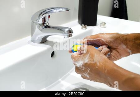 Schwarze Frau, die sich gewissenhaft die Hände mit Seife wäscht und ihre Nägel mit einem Pinsel putzt. Selektiver Fokus auf Hände. Desinfektion. Hygienekonzept. Stockfoto