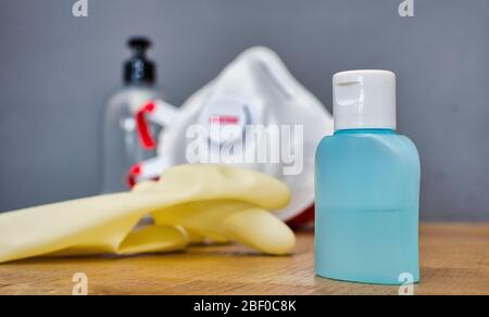 Selektiver Fokus auf das Desinfektionsgel. Verschwommener Hintergrund mit einer Plastikseifenflasche, einer FFP3 Maske und Handschuhen auf einem Holztisch. Coronavirus-Prävention. Stockfoto