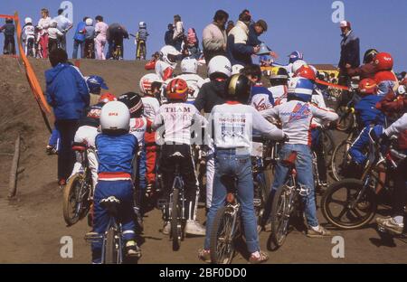 70er Jahre, draußen auf einer Strecke, eine Gruppe von Jungs auf ihren Rädern am Start warten, um am BMX-Rennen teilnehmen. Einige tragen volle Kit, einige nur ein Top und Demin Jeans, aber alle von ihnen haben Schutzhelme. BMX Racing ist ein Off-Road-Radrennsport und der Name 'BMX' kommt von der Kürzung des 'Fahrrad-Motorocross'. Der Sport begann in den frühen 70er Jahren. Stockfoto