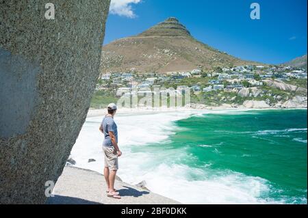 Ein Mann blickt auf den wunderschönen Blick auf den Strand von Llandudno, Kapstadt, Western Cape Province, Südafrika, der ein beliebter Ort für Surfer ist. Stockfoto