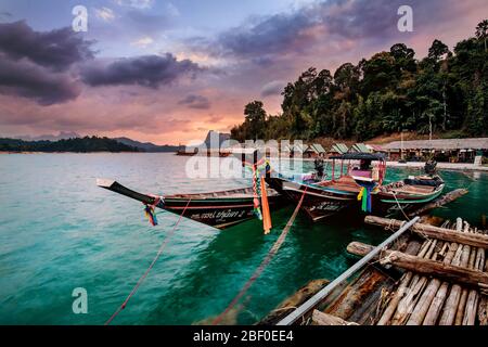 Schwimmende Bungalows und Langschwanzboot bei Sonnenaufgang im Khao Sok Nationalpark, Thailand. Stockfoto