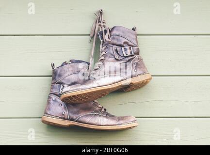 Ein Paar alte abgenutzte Lederschuhe hängen an der Holzwand, verlassene Stiefel Stockfoto