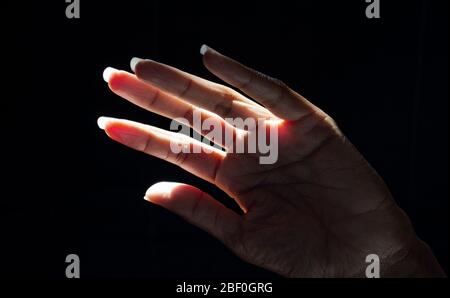 Schwarze Frau hebt ihre Hand, um sich vor den harten Strahlen der Sonne zu schützen. Low-Key-Fotografie. Hope Konzept. Stockfoto