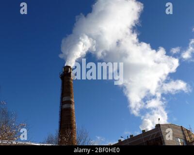 Rohre einer alten Fabrik werfen Wolken von giftigem weißem Rauch in den Himmel, die die Atmosphäre schädigen. Urbaner Smog aus Rauch aus Kesselhäusern. Weißer Rauch aus einem Kamin gegen einen blauen klaren Himmel. Stockfoto