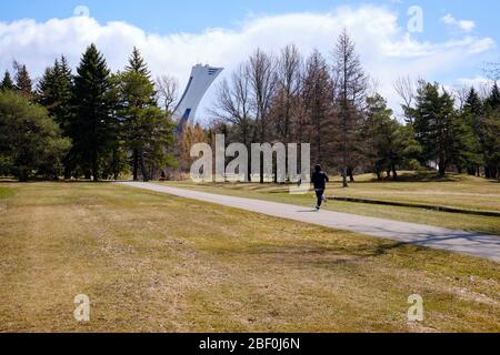Montreal, Quebec, Kanada. April 2020. Menschen, die die sozialen Distanzierungsrichtlinien respektieren, während sie im Maisonneuve Park in Montreal trainieren. Blick auf den Turm des Olympiastadions im Hintergrund Stockfoto