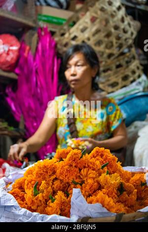 Vertikales Porträt einer Dame, die Blumen für Canang Sari auf dem Pejeng Markt in Bali, Indonesien verkauft. Stockfoto