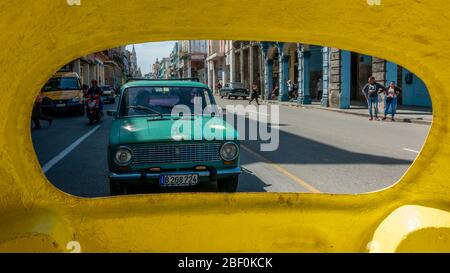 Blick auf ein Paar in einem lada Auto, das hinter einem gelben Cocotaxi durch die Altstadt von Havanna, Kuba fährt Stockfoto