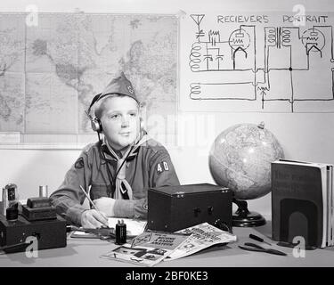 1950ER JAHRE JUNGE SCOUT IN UNIFORM EIN AMATEUR-FUNKER AM SCHREIBTISCH SITZEN OHRHÖRER HÖREN BETRIEB EINES KURZWELLENRADIO - B3736 LEF001 HARS HALBE LÄNGE SCOUTS MÄNNER SCHINKEN TEENAGER JUNGE B & W ERFOLG WEITWINKEL TRÄUME GLÜCK BETREIBER FRÖHLICH ENTDECKUNG HOBBY FREIZEIT AUFREGUNG LEISTUNGSSTARKE ERHOLUNG STOLZ EIN IN GELEGENHEIT BOY SCOUT HIGH TECH THRIFTY KONZEPTIONELL HÖFLICH FREUNDLICH HILFSBEREIT FREUNDLICH REVERENT STILVOLL VERTRAUENSWÜRDIG KOPFHÖRER JUVENILES LOYAL PRE-TEEN JUNGE ENTSPANNUNG AMATEUR VORBEREITET WERDEN SCHWARZ UND WEISS MUTIG KAUKASISCHEN ETHNIZITÄT GEHORSAM ALTMODISCH Stockfoto