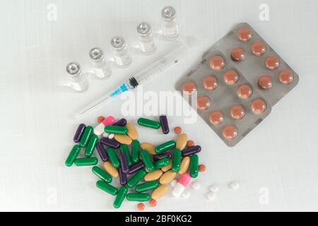 Tabletten und Kapseln, eine Spritze und Fläschchen der Medizin auf einem weißen Tisch. Arzneimittel zur Behandlung des Coronavirus Stockfoto