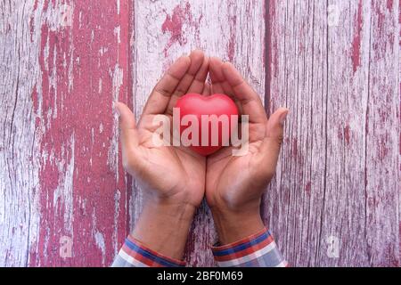 Mann hält rotes Herz in Händen auf Holztisch. Stockfoto