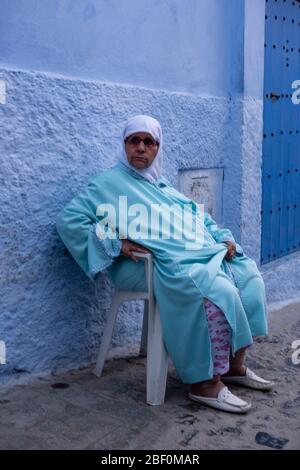 Chefchaouen, Nordmarokko, 10. Juni 2016. Eine Dame in traditioneller marokkanischer Kleidung schaut Passanten an der Tür an. Stockfoto