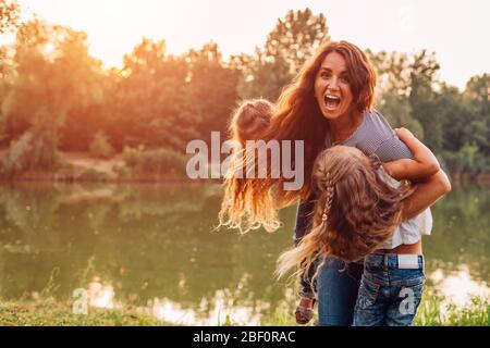 Muttertag. Familie spielen und Spaß am Quellsee haben. Mutter hält und dreht sich um Töchter im Freien. Stockfoto