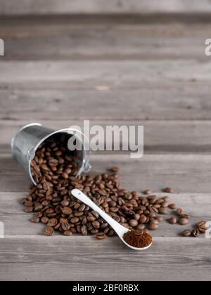 Arabica-Kaffeebohnen in einem kleinen kleinen kleinen Eimer. Gemahlener Kaffee in einem weißen Keramiklöffel auf Holzgrund Stockfoto