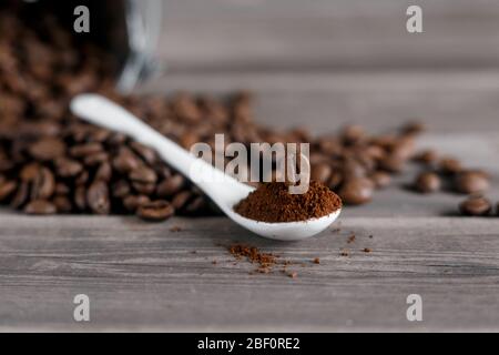 Weißer Keramiklöffel mit gemahlenem Kaffee auf Holzgrund gebratene Arabica-Körner. Stockfoto