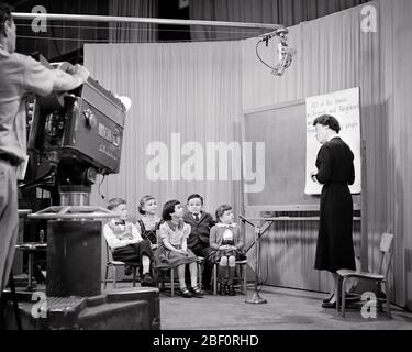 1950ER MANN BETRIEB FERNSEHKAMERA ZEIGT FRAU LEHRER INSTRUCTING LESEKLASSE FÜR ERSTE BIS DRITTE KLASSE SCHÜLER - S3734 HAR001 HARS ERSTE GEMEINSCHAFT URBAN ALTE ZEIT NOSTALGIE MEDIEN ALTE MODE 1 DURCH JUGENDLICHE KOMMUNIKATIONSTECHNOLOGIE TEAMWORK LEBENSSTIL FÜNF FRAUEN 5 JOBS ZEIGEN KOPIERRAUM VOLLER LÄNGE DAMEN PERSONEN FÜRSORGLICHEN MÄNNER UNTERHALTUNG B & W-FERNSEHER DARSTELLENDE KUNST WEITWINKEL SKILL GRADE BERUF FÄHIGKEITEN BETRIEB RUNDFUNK ENTDECKUNG KUNDENDIENST WISSEN FORTSCHRITT BILDUNGSMÖGLICHKEIT AUTORITÄT BERUFE DRITTE INSTRUCTING HIGH-TECH-VERBINDUNG KONZEPTIONELL Stockfoto