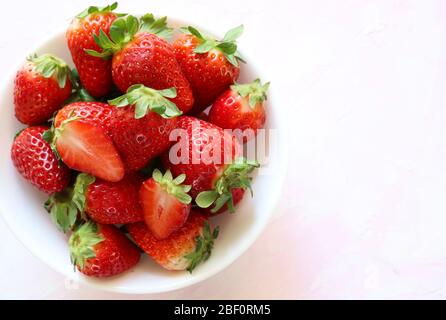 Konzept der gesunden Früchte. Frische Erdbeeren in einer weißen Schüssel auf weißem Hintergrund mit Nuancen von rosa isoliert. Draufsicht. Stockfoto