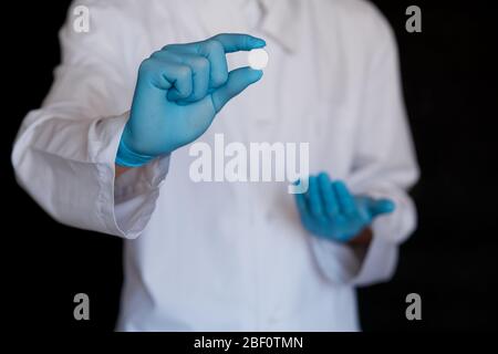 Viele kleine weiße Pillen in den Händen eines Arztes, der medizinische blaue Einweghandschuhe trägt. Hände nehmen eine Tablettenform. Stockfoto