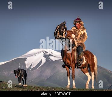 Mongolischer Adlerjäger, Kasachisch zu Pferd mit ausgebildetem Adler vor schneebedeckten Bergen, Provinz Bajan-Oelgii, Mongolei Stockfoto