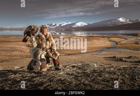 Mongolischer Adlerjäger mit See vor Landschaft mit See und schneebedeckten Bergen, Bajan-Oelgii Provinz, Mongolei Stockfoto