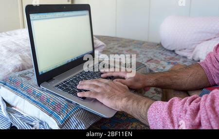 Provisorische Arbeitsplatz, wo ein Erwachsener Mann arbeitet von seinem Schlafzimmer mit Kissen, um seinen Laptop während der covid-19 Pandemie, Schweden zu unterstützen Stockfoto