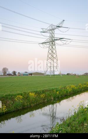 Hochspannungs-Pylon mit Stromleitungen für den Transport von Strom in der niederländischen Landschaft bei Dämmerung Stockfoto