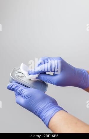 Handschuppen reinigen eine Dose Konserven nach dem Lebensmitteleinkauf, um die Ausbreitung des Coronavirus zu verhindern Stockfoto