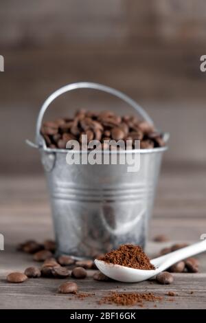 Arabica-Kaffeebohnen in einem kleinen kleinen kleinen Eimer. Gemahlener Kaffee in einem weißen Keramiklöffel auf Holzgrund Stockfoto
