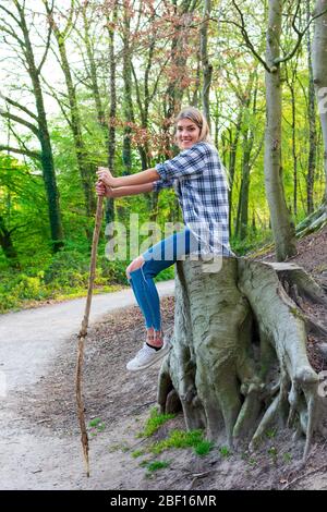 Junge Frau sitzt lächelnd auf einem großen Baumstumpf im Wald. Standort: Deutschland, Nordrhein-Westfalen Stockfoto