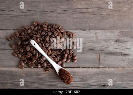 Weißer Keramiklöffel mit gemahlenem Kaffee auf Holzgrund gebratene Arabica-Körner. Stockfoto