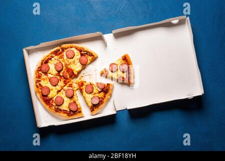 Pizza in einer Pappschachtel auf einem blauen Tisch, oben gesehen. Lieferung Pizza Box mit heißen Pizza Salami in 6 gleiche Portionen geschnitten. Stockfoto