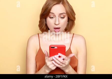Porträt von schockierten oder ängstlich junge Frau suchen und schreiben Nachricht auf Smartphone mit offenem Mund, hat Gesichtsausdruck überrascht, über b isoliert Stockfoto