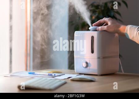 Mann mit Aroma Öl Diffusor auf dem Tisch, Dampf aus dem Befeuchter, selektive Fokussierung. Befeuchtung der Luft in der Wohnung während der Zeit des selbst-ist Stockfoto