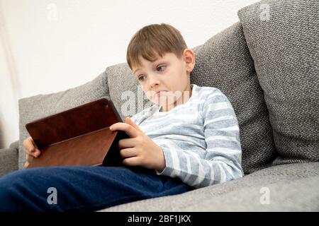 Erstaunte junge Blick in einem Tablet-pc-Bildschirm. Fernunterricht Online-Bildung. Niedlichen kaukasischen Jungen tun Hausaufgaben zu Hause während Quarantäne von Stockfoto