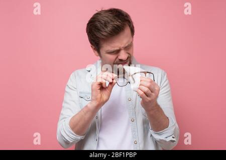 Junger kaukasischer Mann, der seine Gläser abwischt und von Staub auf der rosa Wand reinigt. Stockfoto