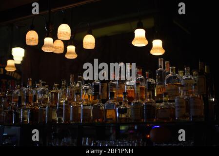 Deckenleuchten beleuchten eine Vielzahl von alkoholischen Spirituosen in Flaschen, die die Wand in einer Bar auskleiden Stockfoto