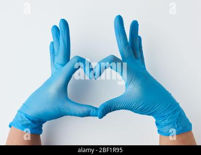 Zwei Hände aus blauem Latex sterile medizinische Handschuhe zeigt eine Geste des Herzens auf einem weißen Hintergrund, Konzept der Güte, Hilfe und Freiwilligenarbeit Stockfoto