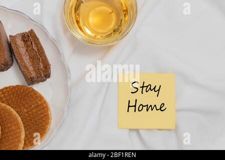 Bleiben Sie zu Hause Phrase auf gemütlichen Hause Hintergrund mit einer Tasse Tee und Süßigkeiten. Selbstisolierung Motivation während COVID-19 Ausbruch Konzept Stockfoto