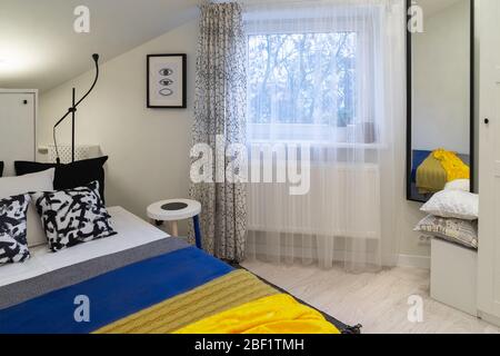 Teil eines kleinen gemütlichen neu eingerichteten Schlafzimmers im Dachgeschoss eines alten Hauses. Überwiegend weiß und schwarz mit einem Akzent von blauen und gelben Bettüberwürfen. Stockfoto