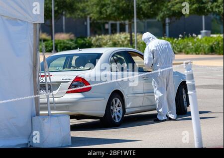 Sugar Land, Texas - 16. April 2020: In voller Schutzkleidung gekleidet sammelt ein Gesundheitsarbeiter Informationen von älteren Paaren, die in ihrem sitzen Stockfoto