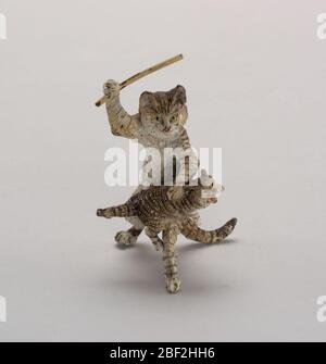 Katze und Kätzchen. Graue, schwarze und weiße, gestromte Katze, die auf den Hinterbeinen steht, hält einen hochgepriesenen Stock über einem über dem Knie liegenden Mähen, als wäre es ein Spanking. Stockfoto