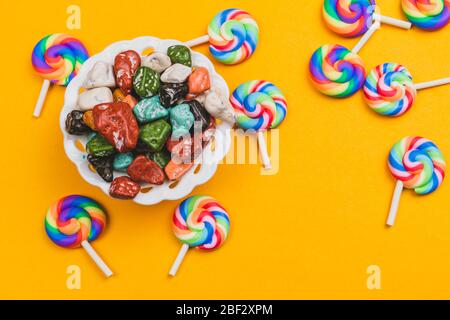 Lutscher auf gelbem Hintergrund. Bonbonschale mit Süßigkeiten in Form von farbigen Steinen. Bunte Bonbons Stockfoto