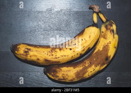 Überreife Bananen mit Flecken. Früchte liegen auf schwarzem Holztisch Stockfoto