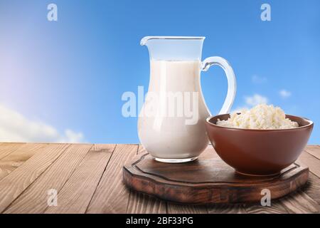 Schüssel mit Quark und Krug Milch auf Holztisch gegen blauen Himmel Stockfoto