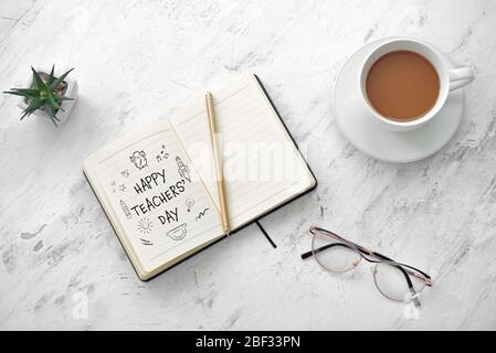 Offenes Notizbuch mit Text HAPPY TEACHER'S DAY, Gläser und Tasse Kaffee auf dem Tisch Stockfoto