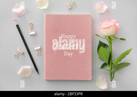 Notizbuch mit Text HAPPY TEACHER'S DAY, Bleistift und Rosenblüte auf grauem Hintergrund Stockfoto