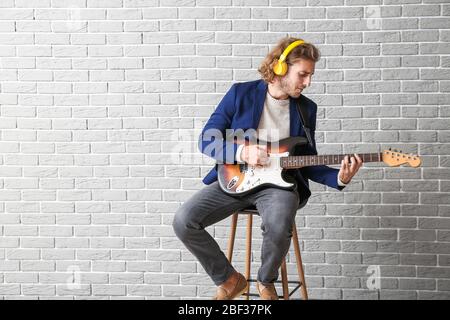 Mann, der Gitarre gegen Ziegelwand spielt Stockfoto